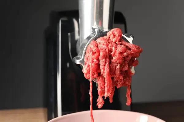 Electric meat grinder with beef mince against grey background, closeup