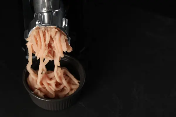 Electric meat grinder with chicken mince on black table. Space for text