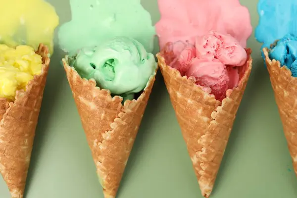 Melted ice cream in wafer cones on pale green background, flat lay