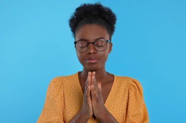 Elleri sımsıkı bağlı bir kadın açık mavi arka planda Tanrı 'ya dua ediyor.