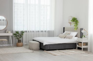 Şık bir yatak odası, geniş konforlu bir yatak ve pencerenin yanında bir şilte.