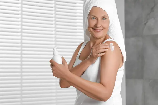 Happy woman applying body cream onto shoulder indoors. Space for text