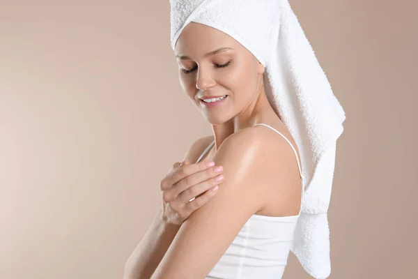 Happy woman applying body oil onto shoulder on beige background, space for text