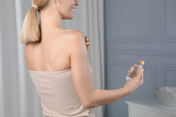 Woman with bottle of body oil in bathroom, closeup. Space for text
