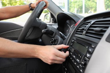 Araba sürerken radyo dinlemek. Aracın ses düğmesini çeviren adam, kapat