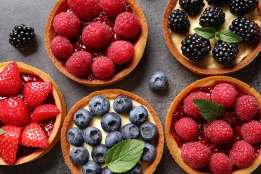 Farklı taze böğürtlenli turtalar gri masada, düz yatıyordu. Tatlı nefis.