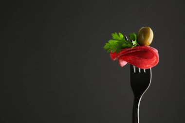 Siyah arka planda lezzetli salam, zeytin ve maydanoz dilimli çatal, metin için boşluk