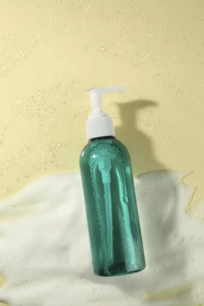 Bottle of face cleanser and white foam on beige background, top view. Skin care cosmetic