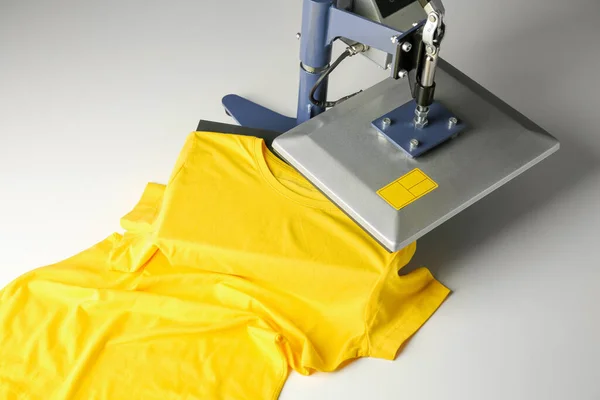 Printing logo. Heat press with yellow t-shirt on white table