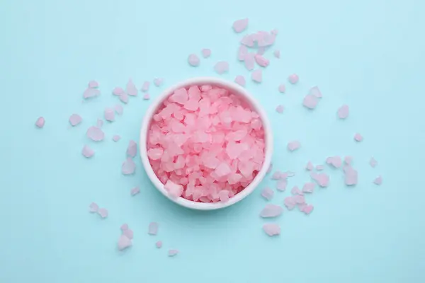 Bowl with pink sea salt on light blue background, top view