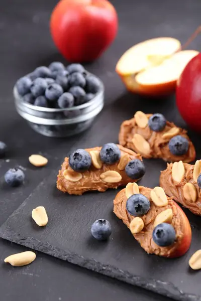 Fresh apples with peanut butter and blueberries on dark table, closeup
