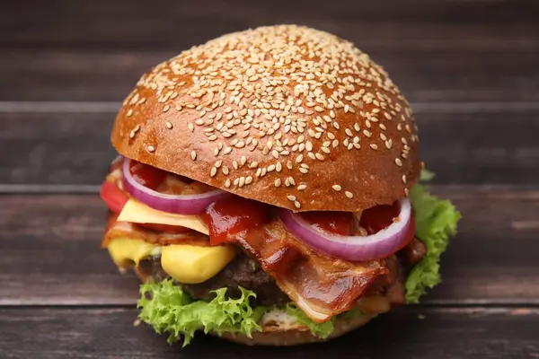 Delicious burger with bacon, patty and vegetables on wooden table, closeup