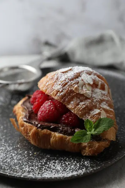 Delicious croissant with raspberries, chocolate and mint on table, closeup