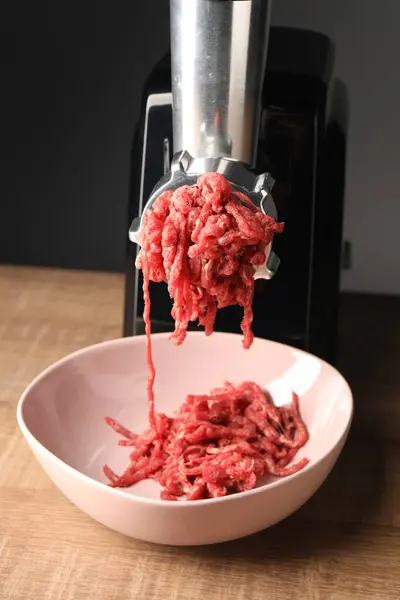 Electric meat grinder with beef mince on wooden table