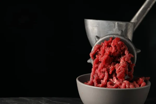 Metal meat grinder with beef mince on black background. Space for text