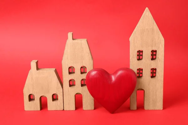 Long-distance relationship concept. Wooden house models and decorative heart on red background