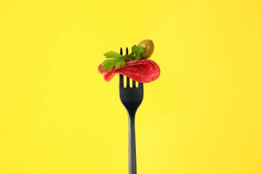 Sarı arka planda lezzetli salamlı, zeytinli ve maydanozlu çatal.