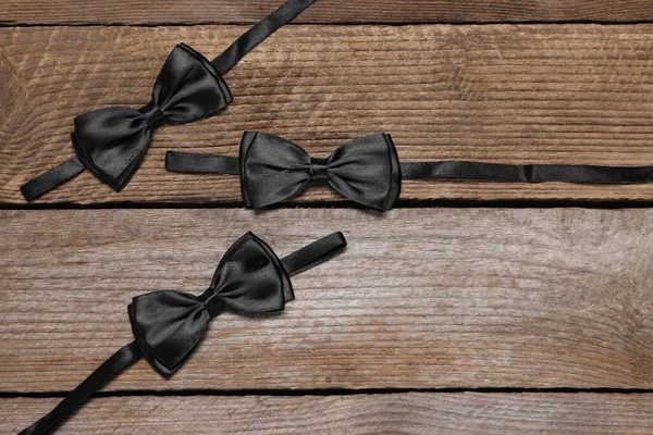 Stylish black bow ties on wooden background, flat lay. Space for text
