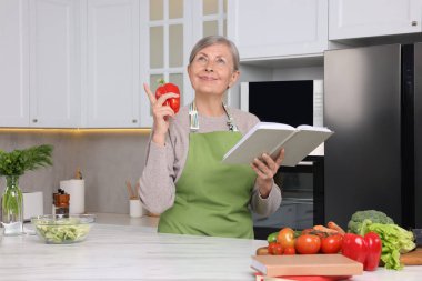 Mutfakta yemek tarifi kitabı ve dolmalık biberli mutlu kadın.