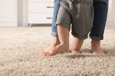Anne, bebeğine evde halıda yürümeyi öğrenirken destek oluyor. Metin için boşluk