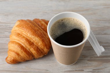 Paket kahve. Lezzetli bir içecekle kağıt bardak ve beyaz ahşap masada kruvasan, yakın plan.