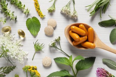 Farklı haplar, şifalı otlar ve çiçekler beyaz ahşap masa, düz yatak. Beslenme takviyeleri