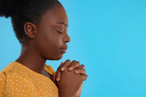 Woman with clasped hands praying to God on light blue background. Space for text
