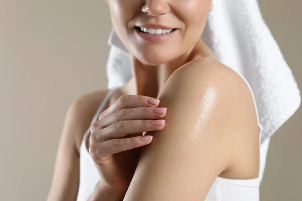 Woman applying body oil onto shoulder on beige background, closeup