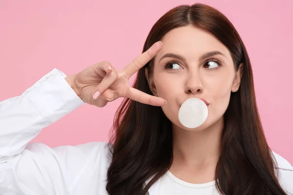 Beautiful woman blowing bubble gum and gesturing on pink background