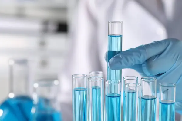 Scientist taking test tube with light blue liquid in laboratory, closeup. Space for text