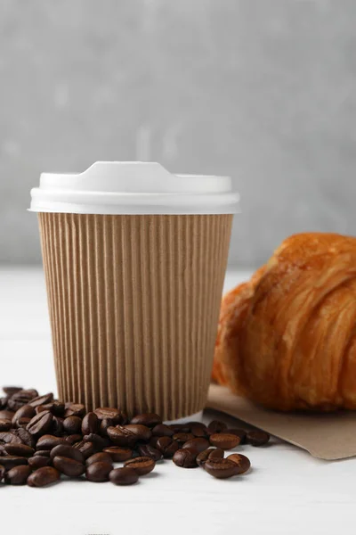 Coffee to go. Paper cup with tasty drink, croissant and beans on white table