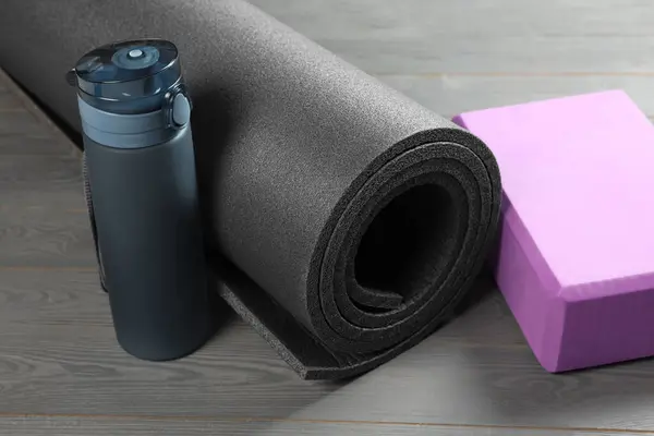 Exercise mat, yoga block and bottle of water on grey wooden floor