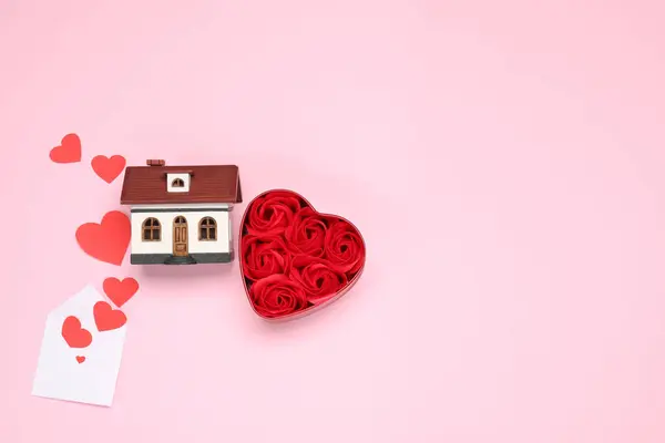 Long-distance relationship concept. House model, rose flowers and paper hearts flying out of envelope, flat lay with space for text