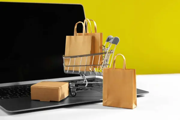 Online store. Laptop, mini shopping cart and purchases on beige table