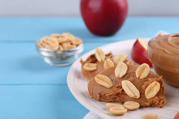 Slices of fresh apple with peanut butter and nuts on light blue wooden table, closeup. Space for text