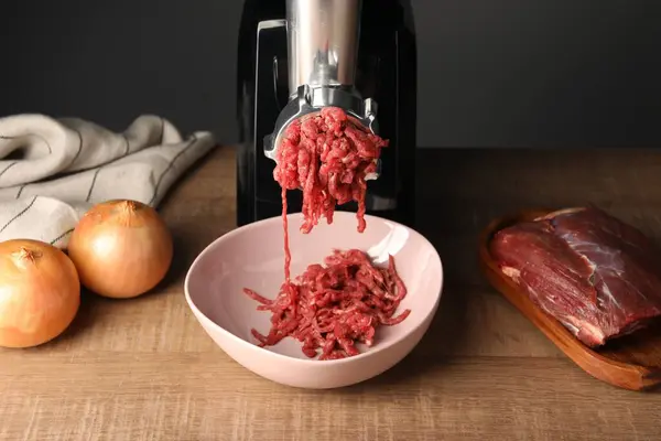 Electric meat grinder with beef mince and onion on wooden table
