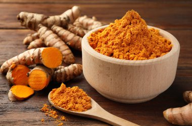 Aromatik zerdeçal tozu ve ahşap masa üzerindeki ham kökler, yakın plan.