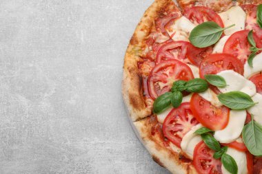 Domatesli lezzetli Caprese pizzası, mozzarella ve açık gri masada fesleğen, üst manzara. Metin için boşluk
