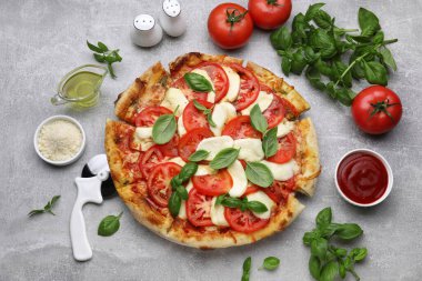 Domatesli lezzetli Caprese pizzası, mozzarella ve açık gri masada fesleğen.
