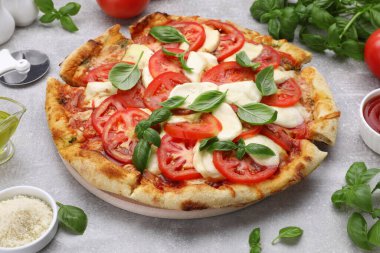 Domatesli Caprese pizzası, mozzarella ve açık gri masada fesleğen.