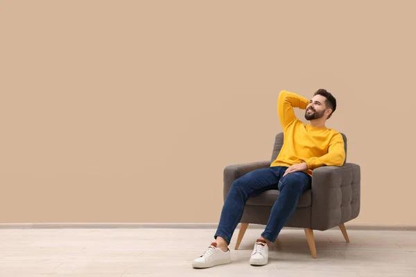 Handsome man relaxing in armchair near beige wall indoors, space for text