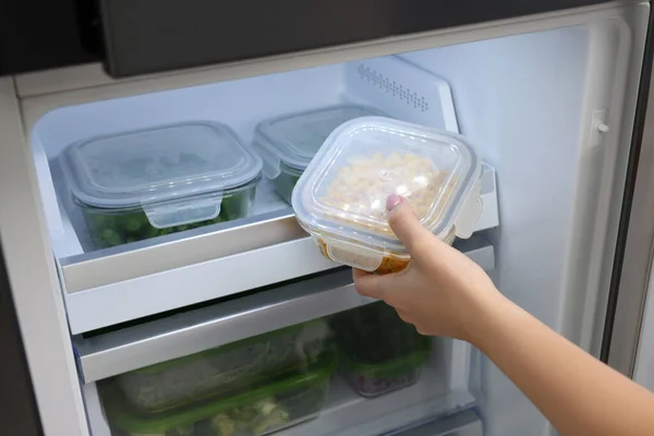 Woman putting container with tasty corn kernels into fridge, closeup. Food storage