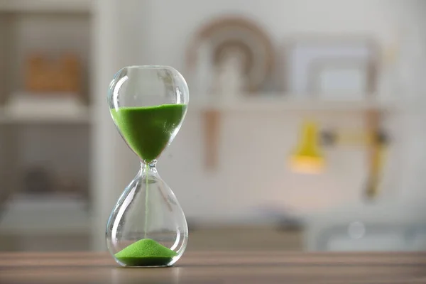 Hourglass with light green flowing sand on table against blurred background. Space for text
