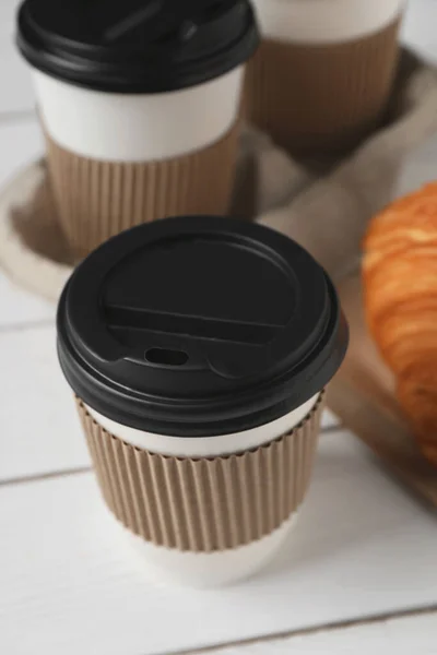 Coffee to go. Paper cups with tasty drink and croissant on white table, closeup