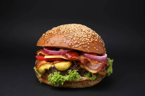 Delicious burger with bacon, patty and vegetables on black background