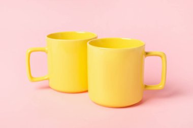Pembe arka planda iki sarı seramik bardak.