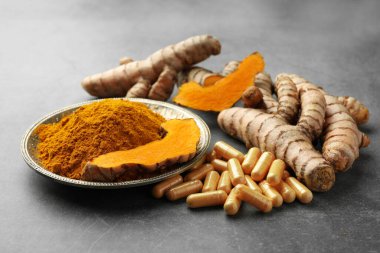 Aromatik zerdeçal tozu, haplar ve gri masadaki ham kökler.