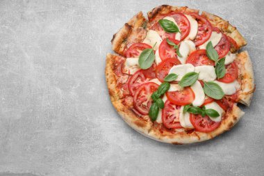 Domatesli lezzetli Caprese pizzası, mozzarella ve açık gri masada fesleğen, üst manzara. Metin için boşluk