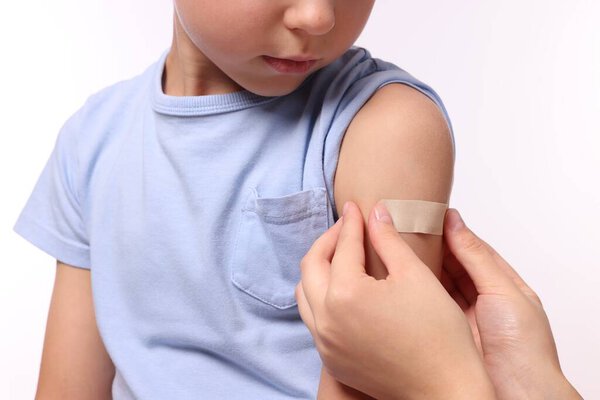 Woman sticking plaster on boy's arm after vaccination against white background, closeup