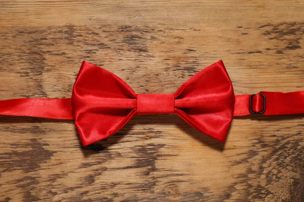 Stylish red bow tie on wooden table, top view